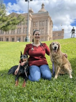 Dr. Sarah kneeling in grass with two dogs